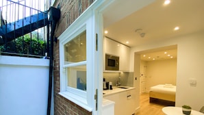 A compact, modern kitchen with a built-in microwave and sink, a small dining area with a table and chair, and a separate bathroom with a shower and toilet. - Star Street Serviced Apartments by Concept Apartments (London)