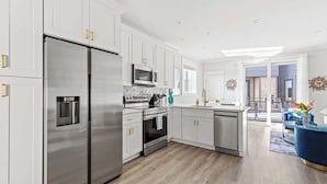 A modern kitchen with stainless steel appliances, white cabinetry, and a wooden floor. - Paradise at The Cove Riverwalk Villas (Wilmington)