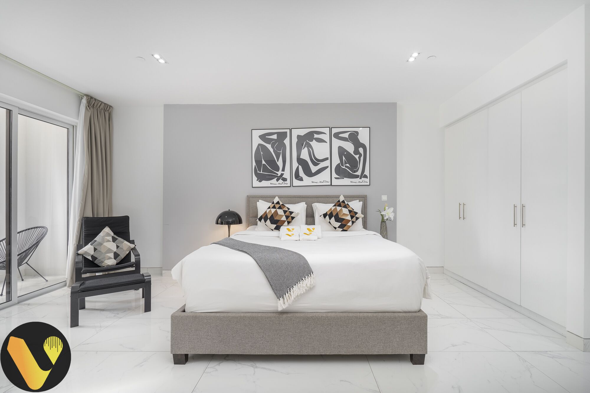 A modern bedroom with a large bed, a chair, and artwork on the wall.