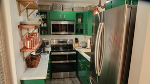 A compact kitchen with green cabinets, a stainless steel refrigerator, a microwave, and an oven. - Navarre Beach "Into the Mystic" Cozy & Unique Townhome (Navarre)