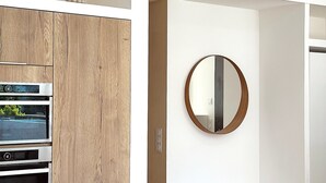 A modern kitchen with wooden cabinetry, built-in appliances, and a round mirror on the wall.