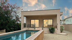 A modern house with a swimming pool, a covered patio, and a garden with flowering plants.