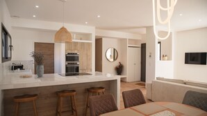 A modern kitchen with a central island, wooden bar stools, and a dining area with a round table.