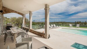 Une terrasse extérieure avec une piscine, des colonnes en pierre, des meubles en osier et un barbecue.