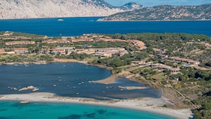 Vue aérienne d’une station balnéaire comprenant plusieurs bâtiments, une plage et un paysage montagneux en arrière-plan.