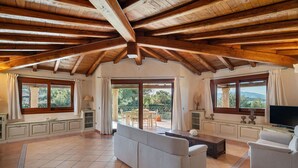 Un salon spacieux avec un haut plafond en bois, de grandes fenêtres et une vue sur l’extérieur.