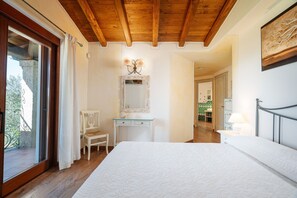 A bedroom with a wooden ceiling, a bed, a dresser, a chair, and a bathroom visible through an open door.