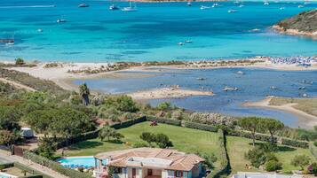A coastal property with a swimming pool, a large house with a tiled roof, and a view of the sea with boats.