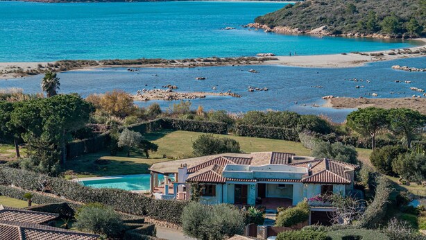 Une villa de style méditerranéen avec piscine, entourée d’une végétation luxuriante et offrant une vue sur une baie aux eaux turquoise.