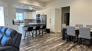 A modern kitchen with a central island, bar stools, and a dining area with a table and chairs. - Modern Mesquite New Home perfect for golfers and families alike. (Mesquite)