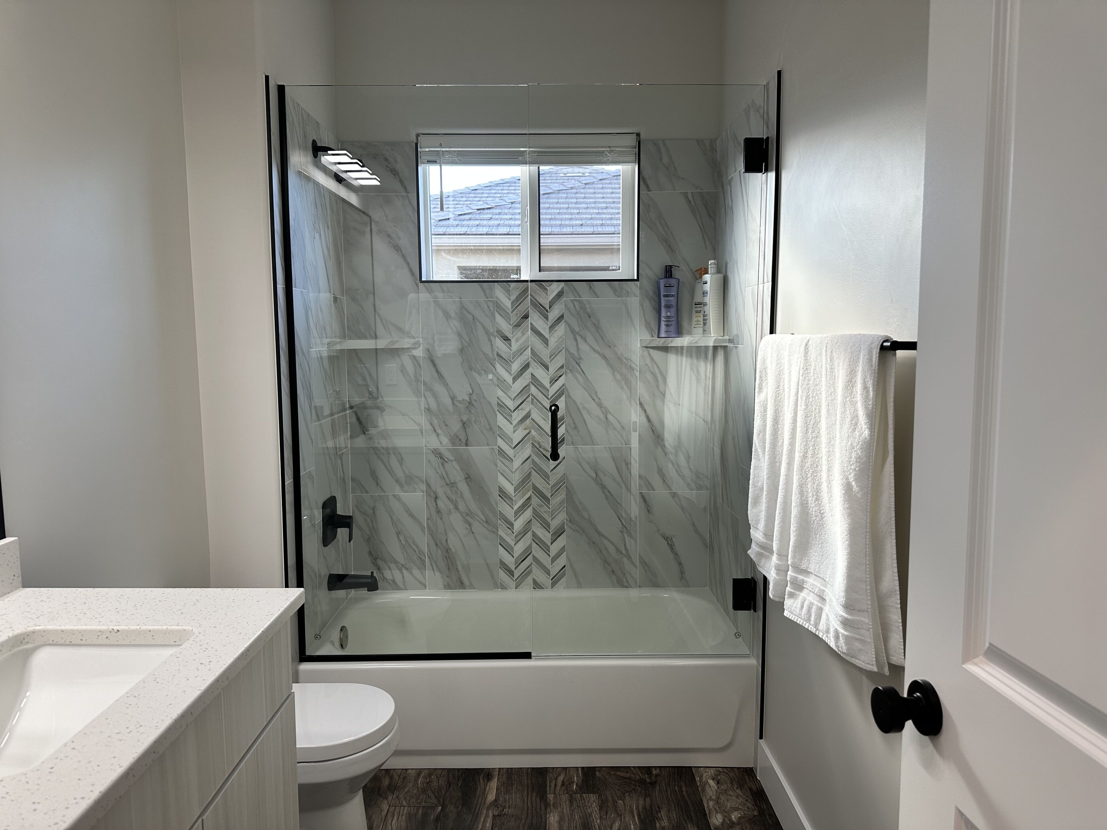 A modern bathroom with a glass-enclosed shower, a white toilet, and a herringbone-patterned tile backsplash.
