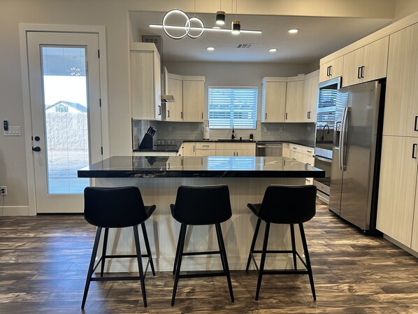 A modern kitchen with a central island, bar stools, stainless steel appliances, and light wood cabinetry.