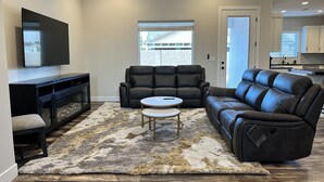 A living room with a black leather sofa, a coffee table, and a TV on a stand. - Modern Mesquite New Home perfect for golfers and families alike. (Mesquite)