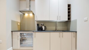 A compact kitchen with white cabinets, a black countertop, and a stainless steel range hood. - Woodview Serviced Apartments by Concept Apartments (London)