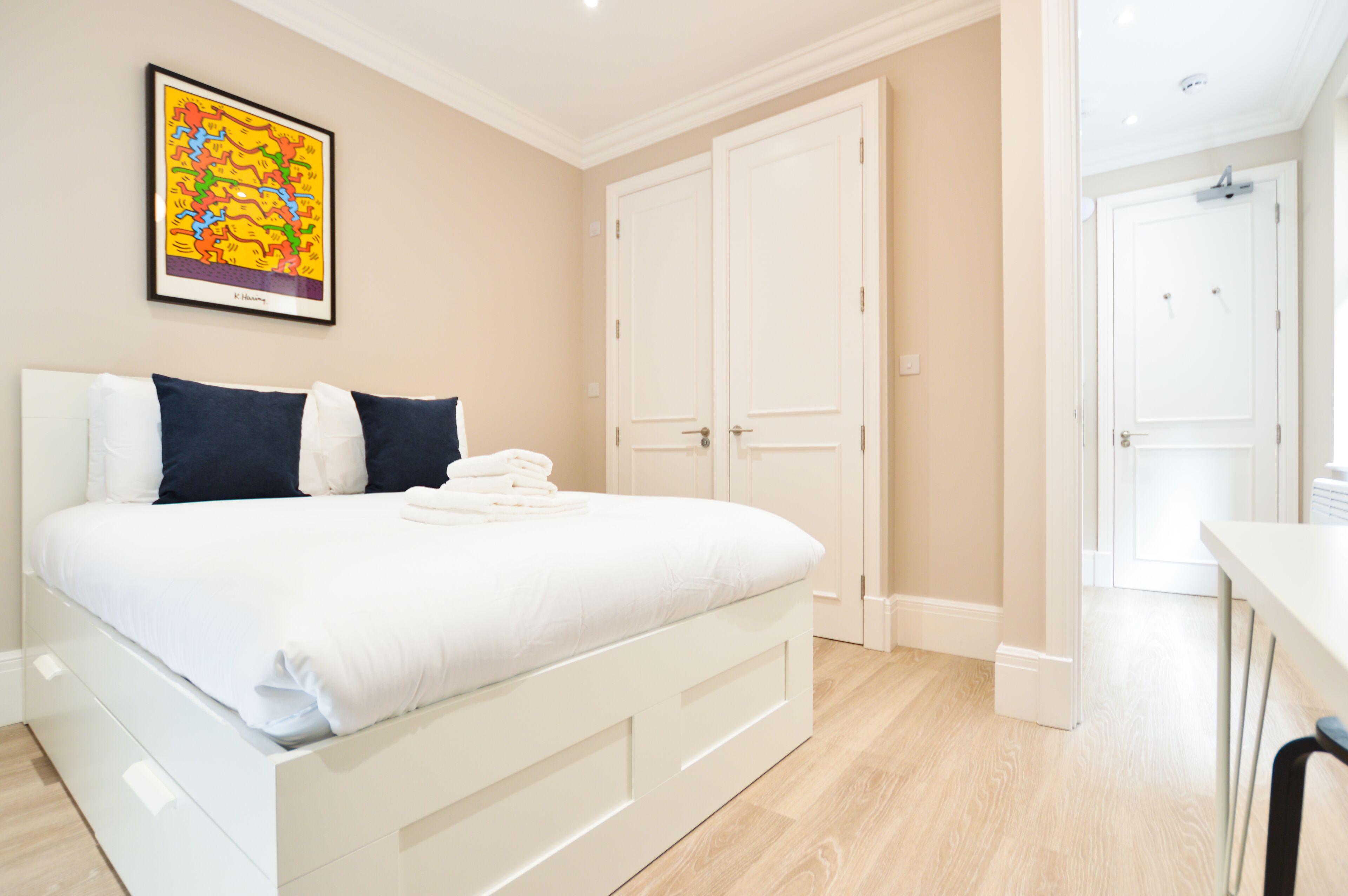 A neatly made bed with white linens and a colorful abstract painting on the wall.
