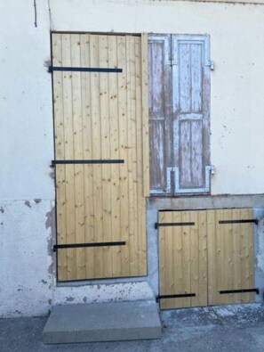 Un edificio con una porta e una finestra in legno, un gradino in cemento e un piccolo sporgere.