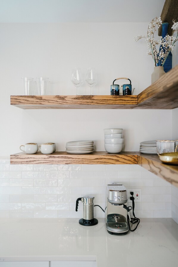 Una cocina con baldosas blancas, estantes de madera y una cafetera.