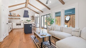 A modern kitchen with wooden beams, a central island, and a dining area with a sofa and coffee table. - Charming New Casita Lower Riviera, Quiet, AC, 6 blocks to State St, Pet-Friendly (Santa Barbara)