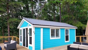A small, single-story house with a blue exterior and white trim, featuring a deck with outdoor furniture.