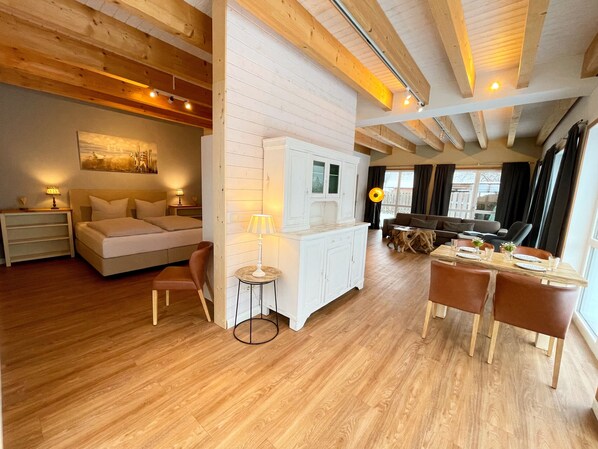A spacious room with a bed, a small table, and a sofa. There is a window with curtains and a view of the outside.