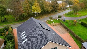 Une maison d’habitation avec un toit en pente, une cheminée visible et une allée pavée.