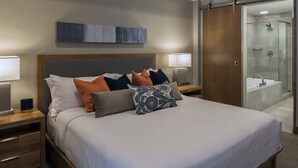 A modern hotel room with a large bed, bedside tables, a nightstand, a wall-mounted artwork, a bathroom with a glass shower enclosure, and a sink. - Ski In/Out! Easy Access-1 Bedroom Breckenridge Master-1.5 Baths-Sleeps 4 (Breckenridge)