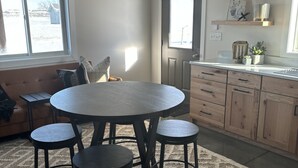 A modern kitchen with a round dining table, bar stools, and wooden cabinets.
