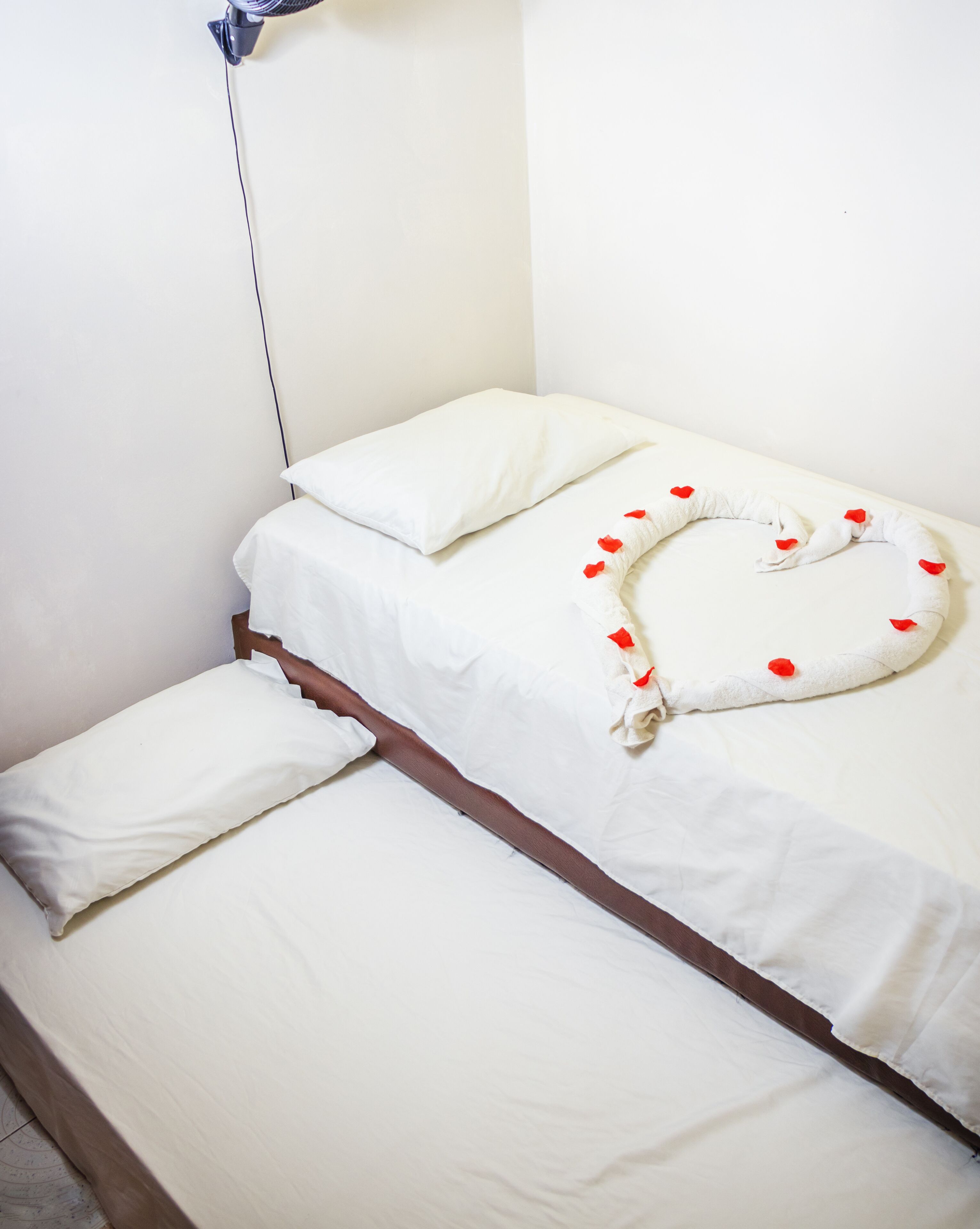 Un letto singolo con biancheria bianca e una composizione di cuscini a forma di cuore.