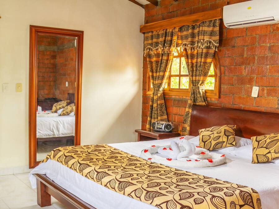 A hotel room with a brick wall, a bed with patterned bedding, a wooden headboard, and a window with curtains.