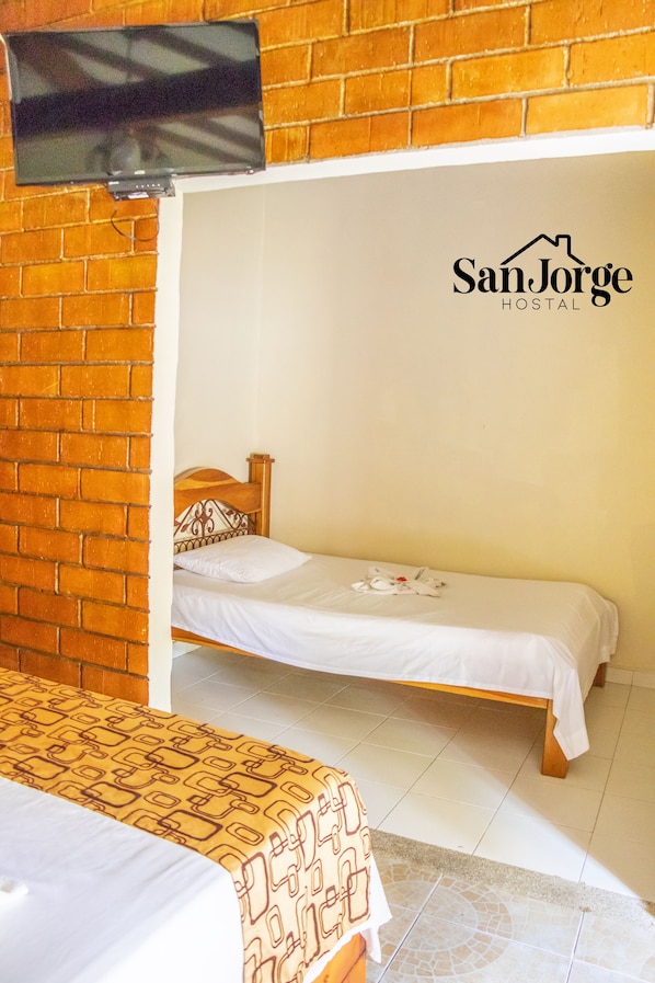 A single bed with a wooden headboard, a TV mounted on a brick wall, and a logo for San Jorge Hostel. - hostal san jorge (Pereira)