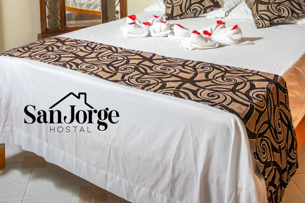 A hotel room with a bed, pillows, a TV mounted on the wall, and a mirror with an arch design.