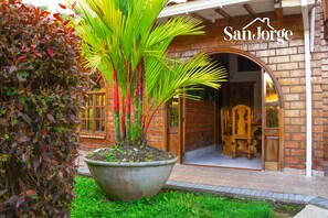 A brick building with a large planter in front, a wooden door, and a sign reading "San Jorge Hostel". - hostal san jorge (Pereira)
