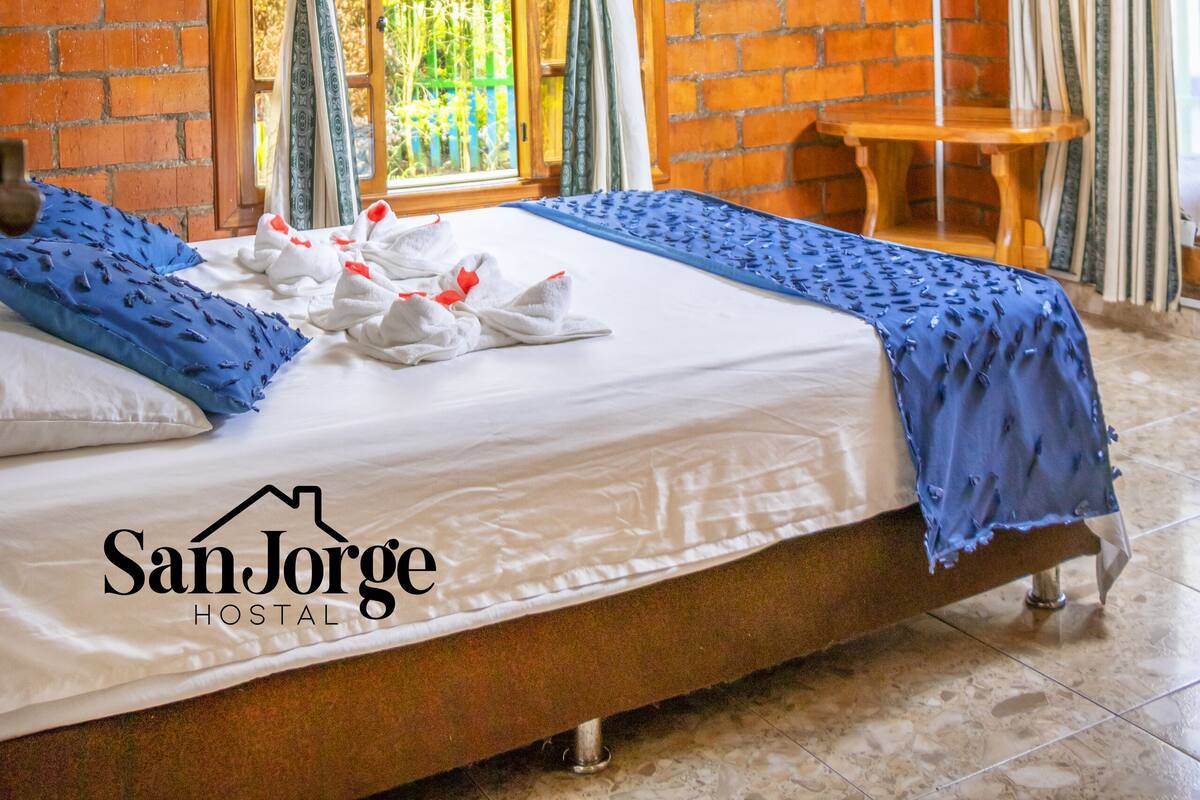A hotel room with a bed, a ceiling fan, a TV, and a brick wall.