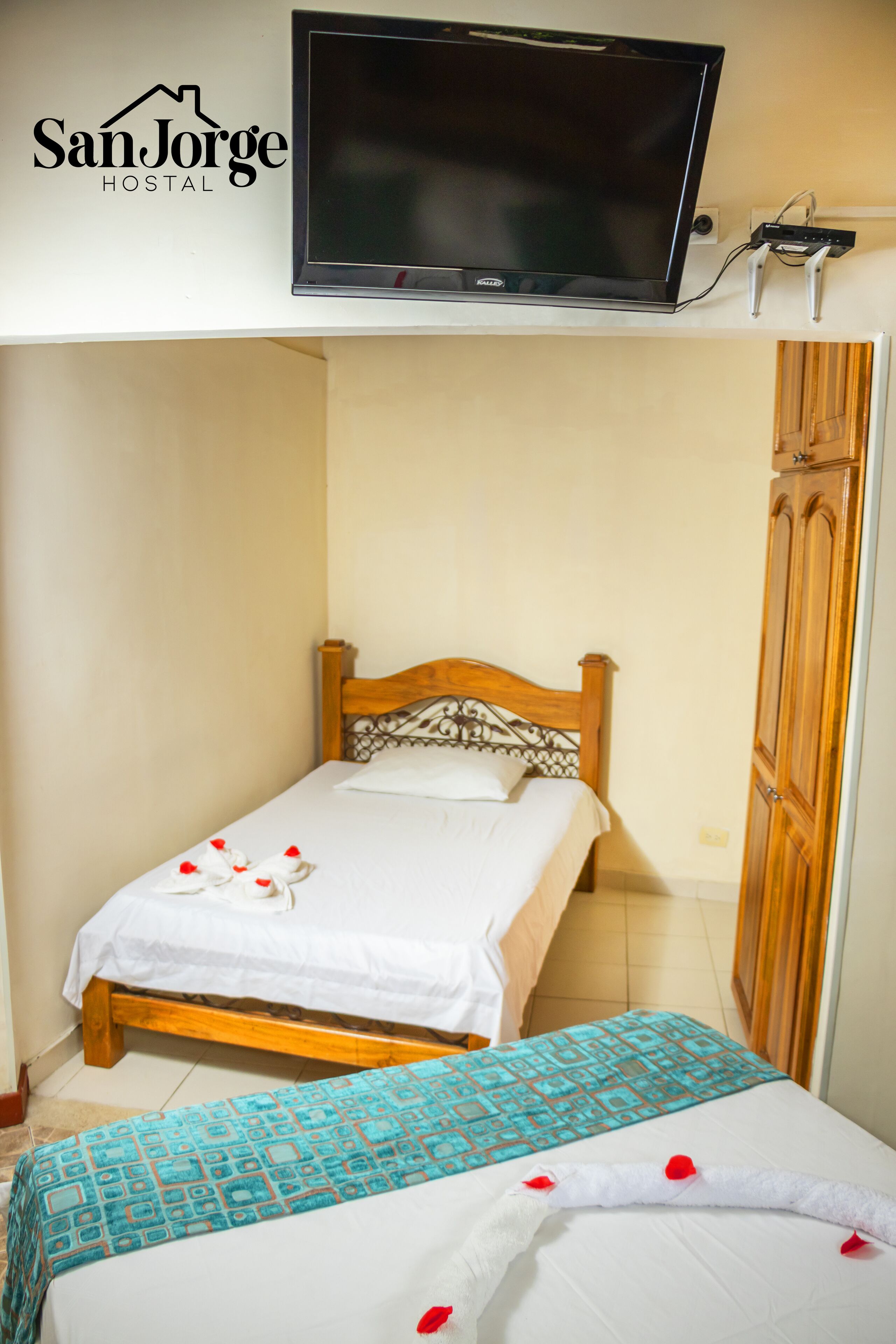 Un lit simple avec une tête de lit en bois et un téléviseur fixé au-dessus.