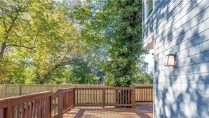 Une terrasse en bois avec une rambarde, entourée d’arbres et d’une maison.