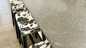Une cuisine dotée d’un plan de travail en granit, de tabourets en peau de vache noir et blanc, d’un réfrigérateur en acier inoxydable et d’une cuisinière blanche.