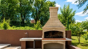 Un four à pizza en briques installé à l’extérieur, avec une table et un évier, le tout entouré d’un jardin aménagé.