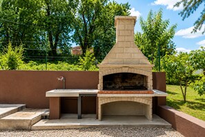 An outdoor brick pizza oven with a table and sink, surrounded by a landscaped garden. - Apartment Magnolia (Istria - Labin) (Labin)