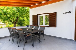 An outdoor patio with a table and chairs, a window with shutters, and a wall with a name sign. - Apartment Magnolia (Istria - Labin) (Labin)