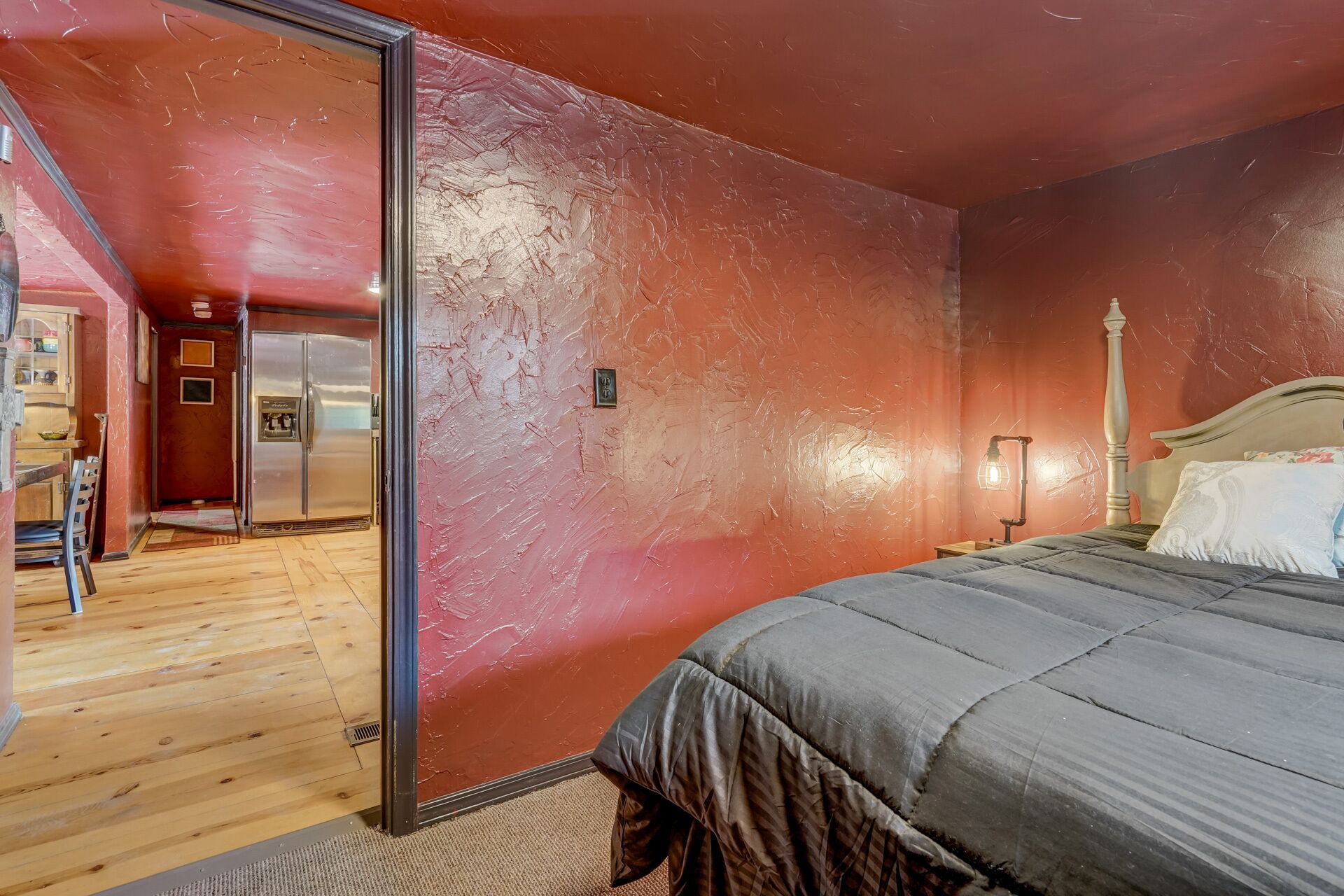 Un dormitorio con una cama, una mesita de noche, una lámpara y una puerta que da a una zona de cocina.
