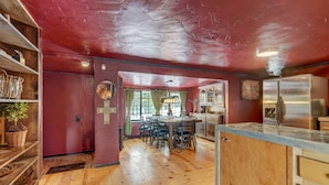 A rustic kitchen with wooden floors, a red ceiling, and a dining area with a table and chairs. - Medieval Manor (Florissant)