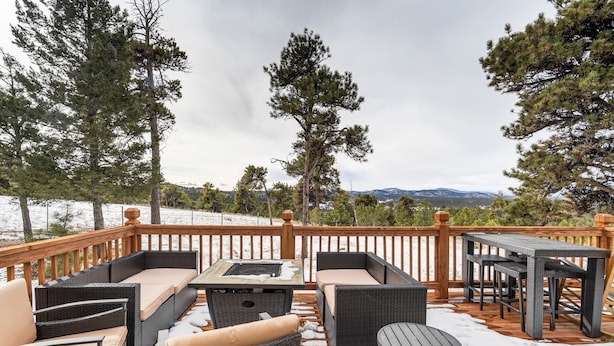 A deck with wicker furniture, a table, and a view of snow-covered mountains. - Medieval Manor (Florissant)