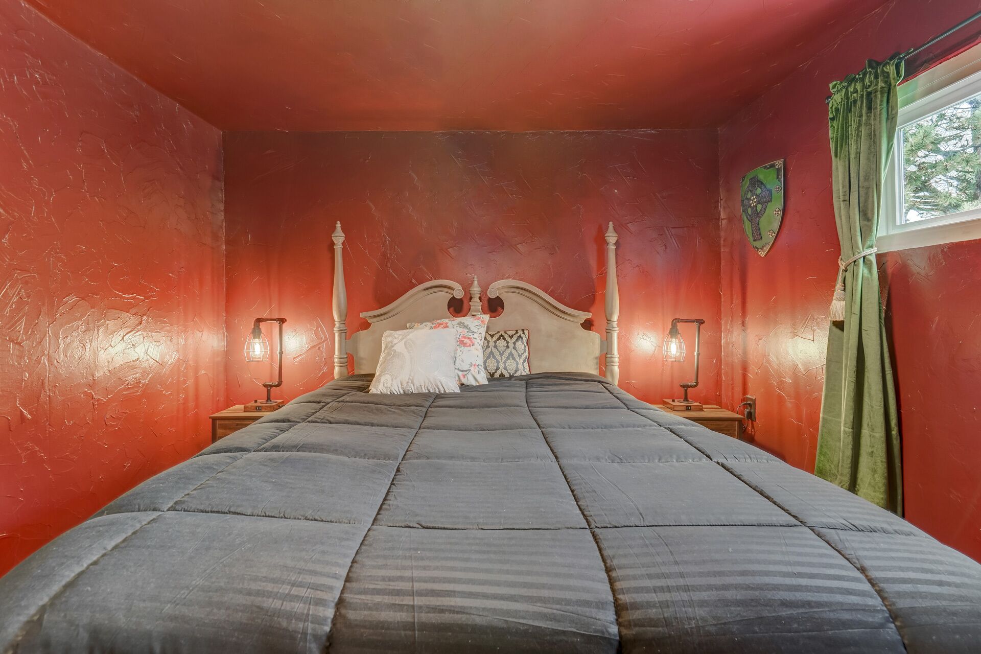 A room with a large bed, two bedside tables, and a window with curtains.
