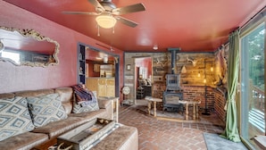 A cozy living room with a leather sofa, a ceiling fan, and a brick fireplace. - Medieval Manor (Florissant)