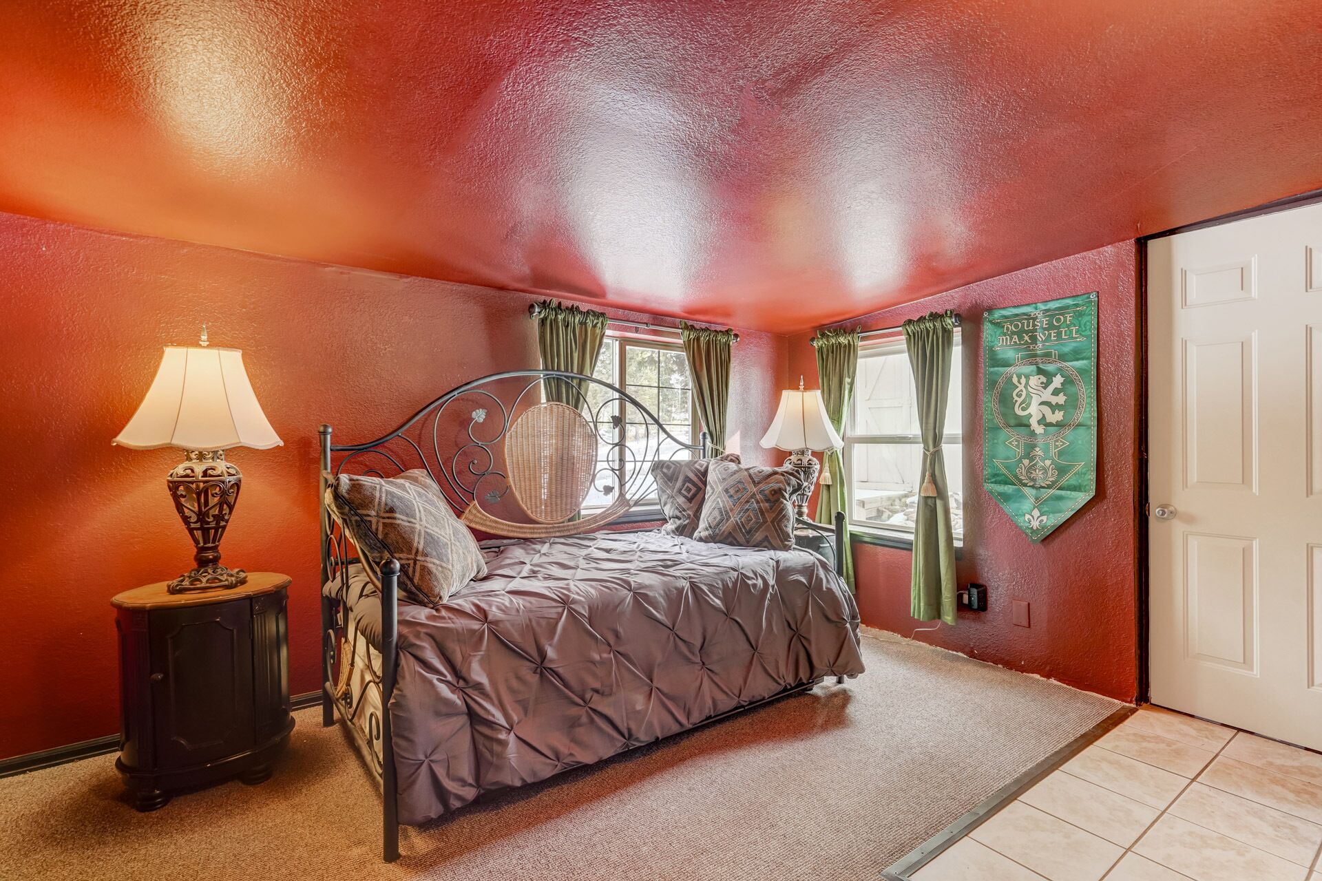 A bedroom with a bed, two bedside lamps, a decorative wall hanging, and a door.