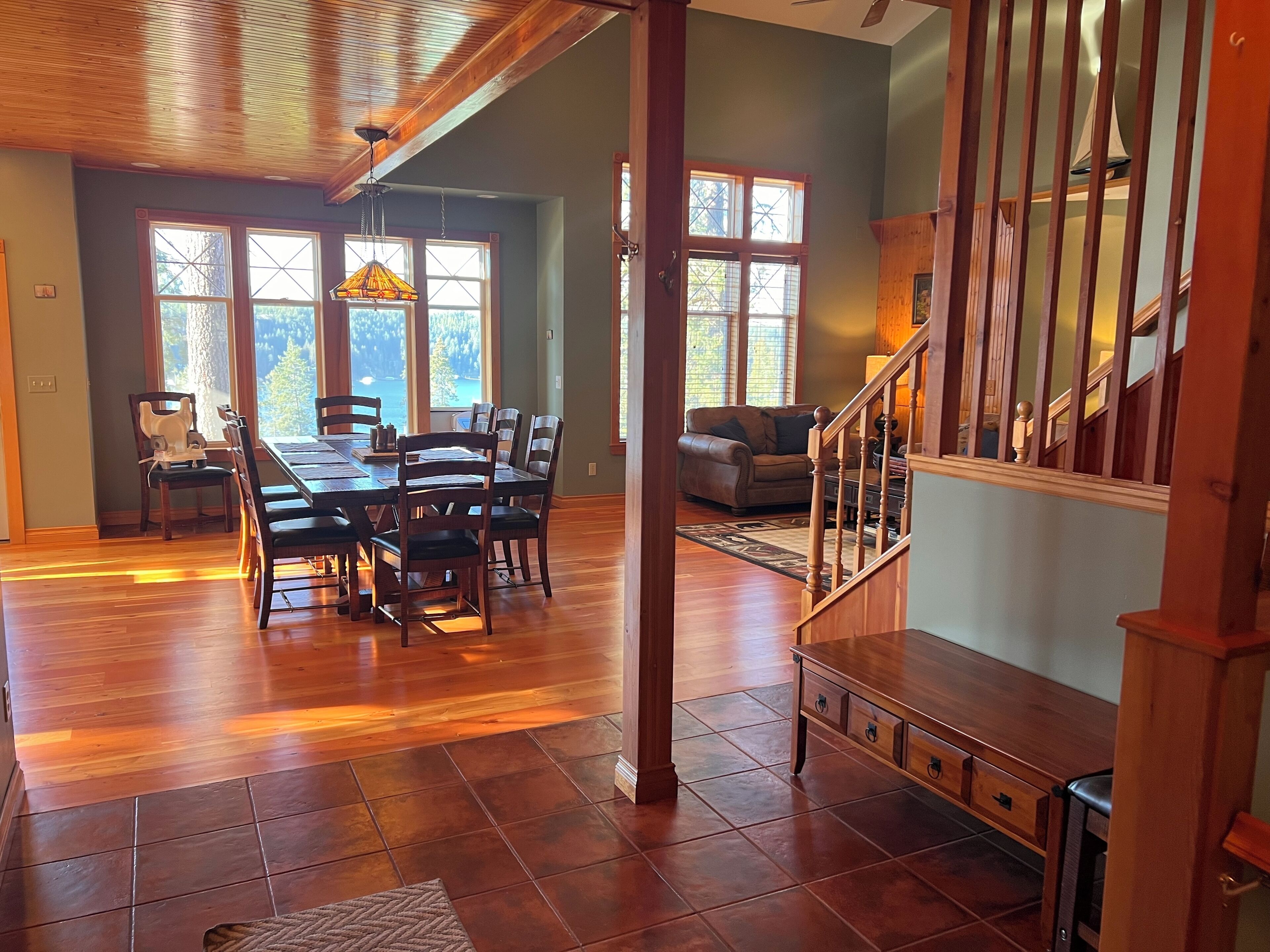 A spacious living area with a wooden dining table and chairs, a leather sofa, and a staircase with wooden railings.
