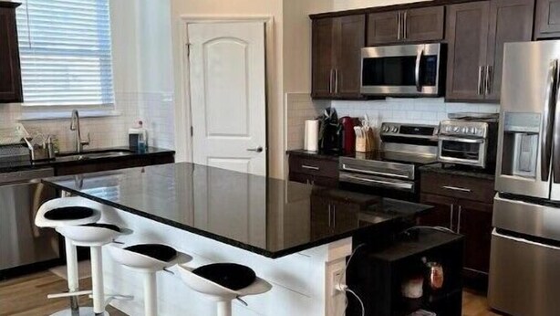 A modern kitchen with a central island, bar stools, stainless steel appliances, and wooden cabinets.