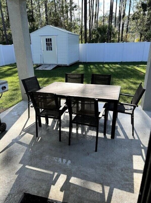 A patio with a wooden table and four chairs, surrounded by a white fence and trees. - Beach Lovers New House! 10 min to beach - 6 guests (Palm Coast)