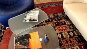 A living room with a flat-screen TV on a white stand, a blue bean bag chair, a beige sofa, and a patterned rug.