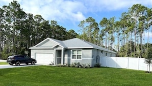 A single-story house with a garage, a well-maintained lawn, and a white fence.